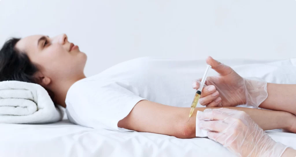 A patient lying flat on a bed as a medical professional provides an infusion as part of at-home immunoglobulin therapy.